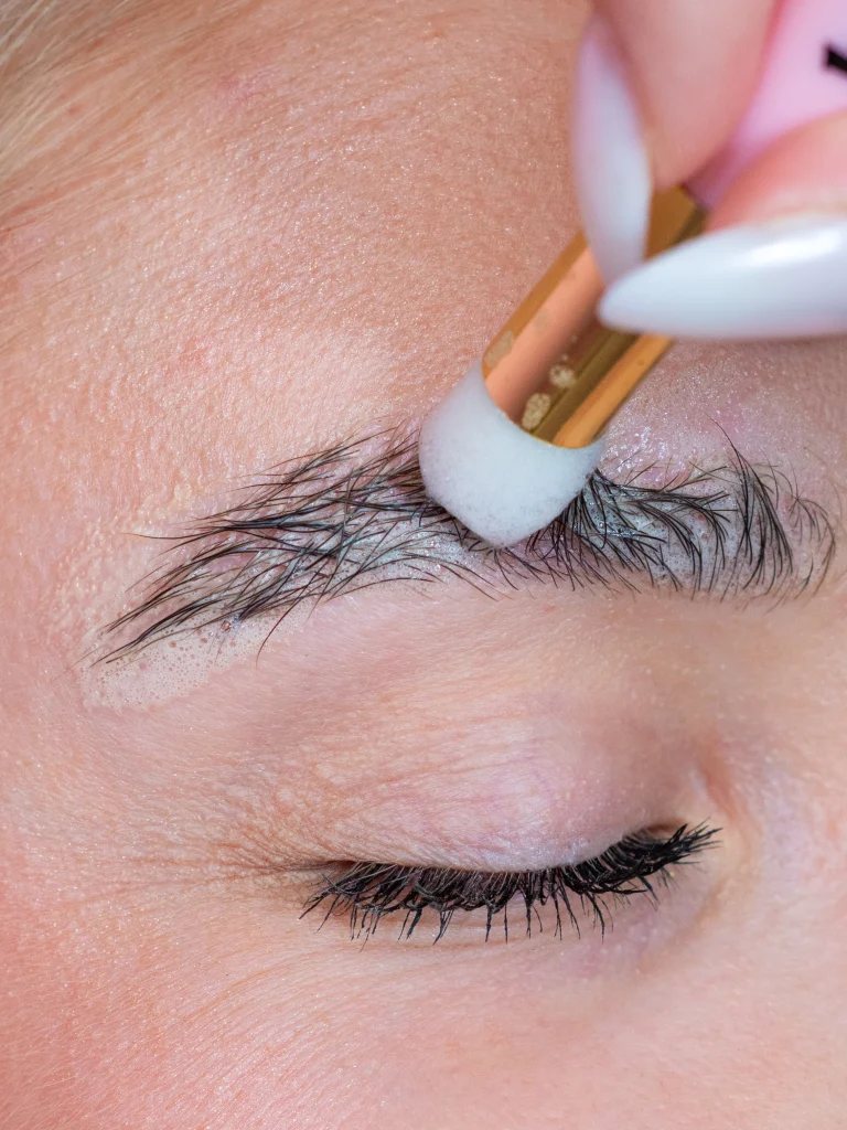 Szemöldök kezelése fehér applikátorral közeli beauty felvételen