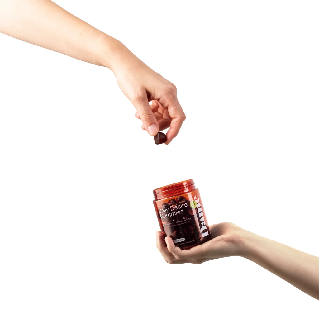 Dame Daily Desire Gummies tégely kézben, felette egy gumicukrot tartó kézzel
