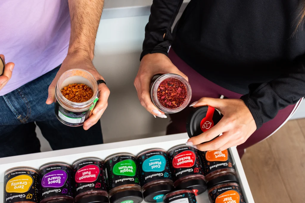 Két ember nyitott myCosmofood termékeket tart a kezében, előttük több termékváltozattal