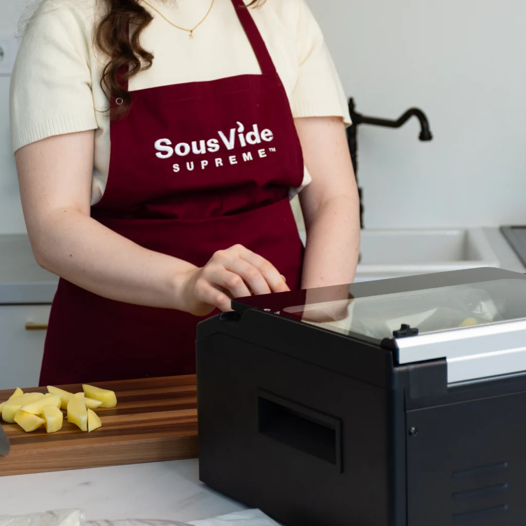 Nő SousVide Supreme kötényben fekete vákuumozó készüléket használ konyhában